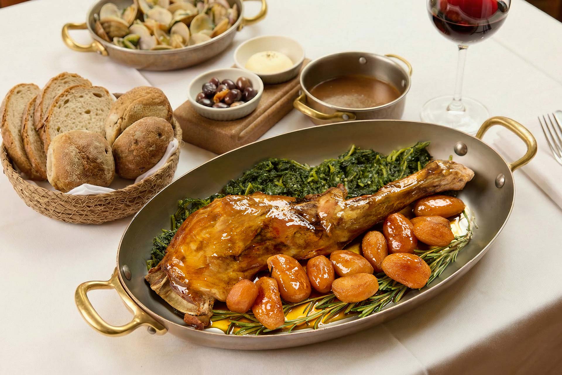 Roast turkey leg with roasted potatoes and greens on a serving platter, rosemary garnish, on a table with wine glasses and bread basket.