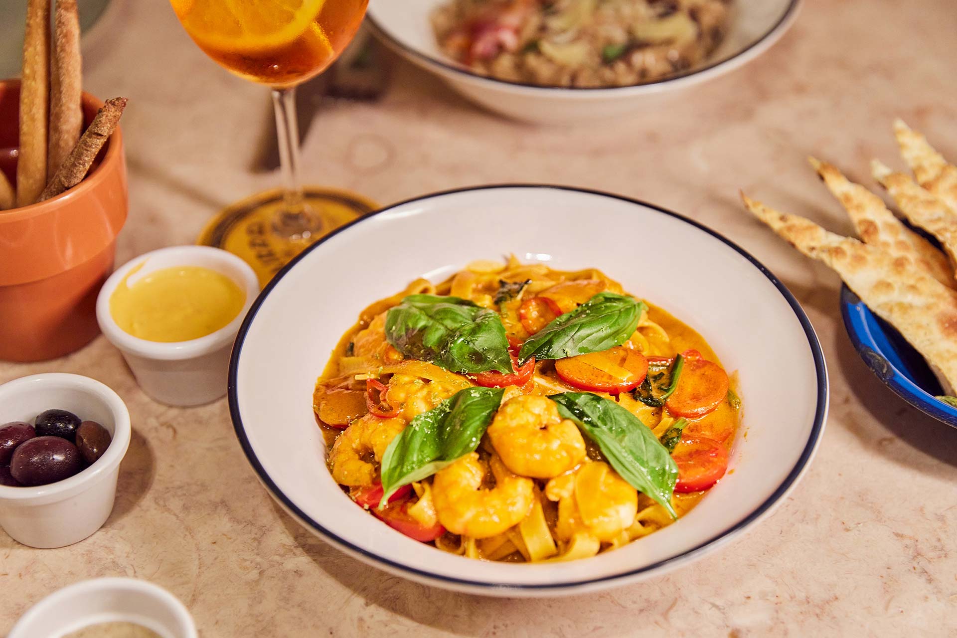 Bowl of pasta with a creamy tomato sauce, colorful vegetables, and fresh basil leaves on a white plate with a dark rim